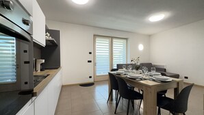 Eine moderne Küche mit Essbereich, mit einem Holztisch für vier Personen, einem eingebauten Backofen und einem Fenster mit Jalousien.