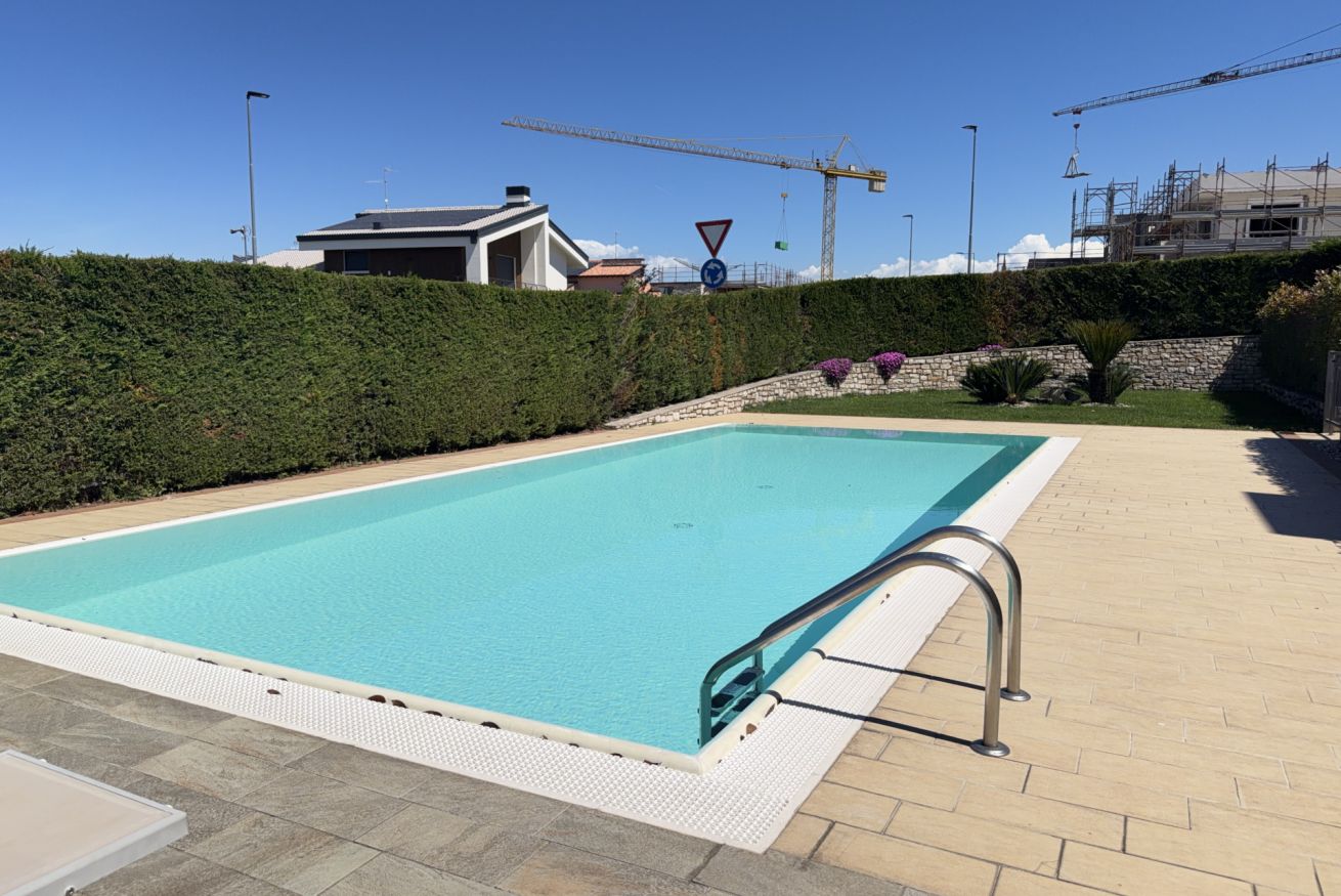 A rectangular swimming pool with a white deck edge, a metal handrail, and a paved walkway.