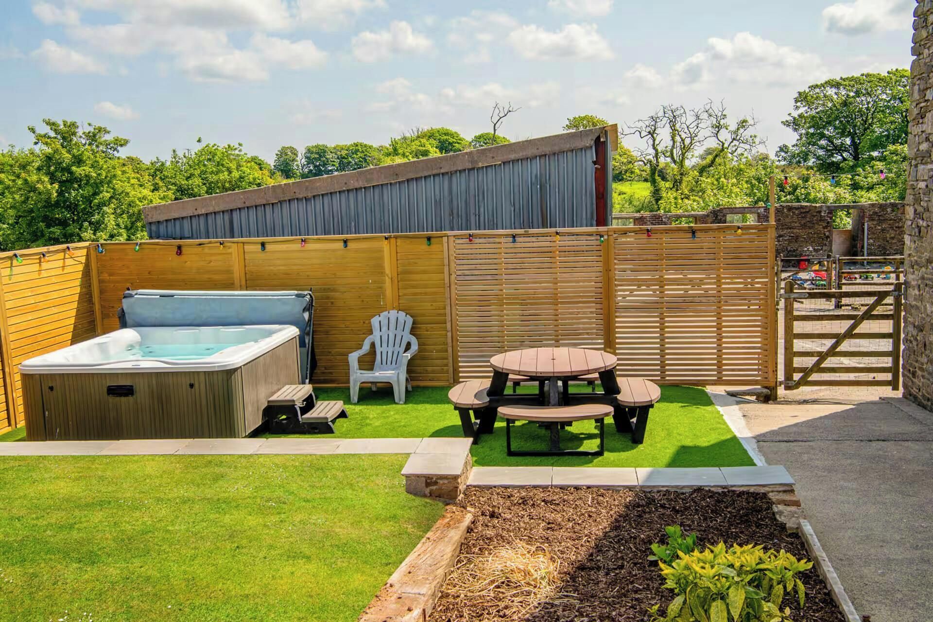 A backyard with a hot tub, a picnic table, and a wooden fence.