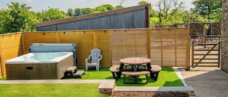 Un patio trasero con jacuzzi, mesa de picnic y cerca de madera.