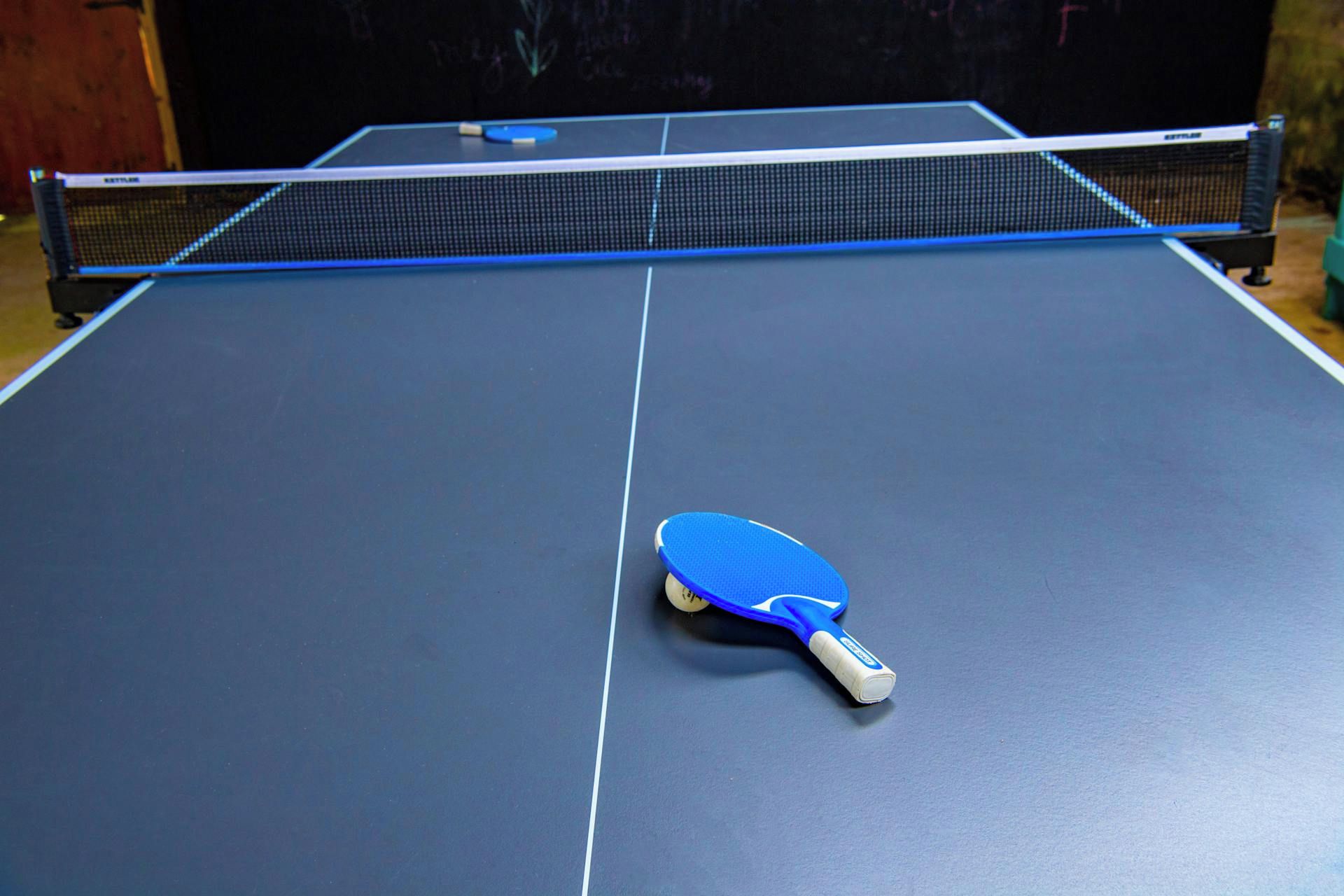 Une table de ping-pong avec un filet et une raquette bleue.