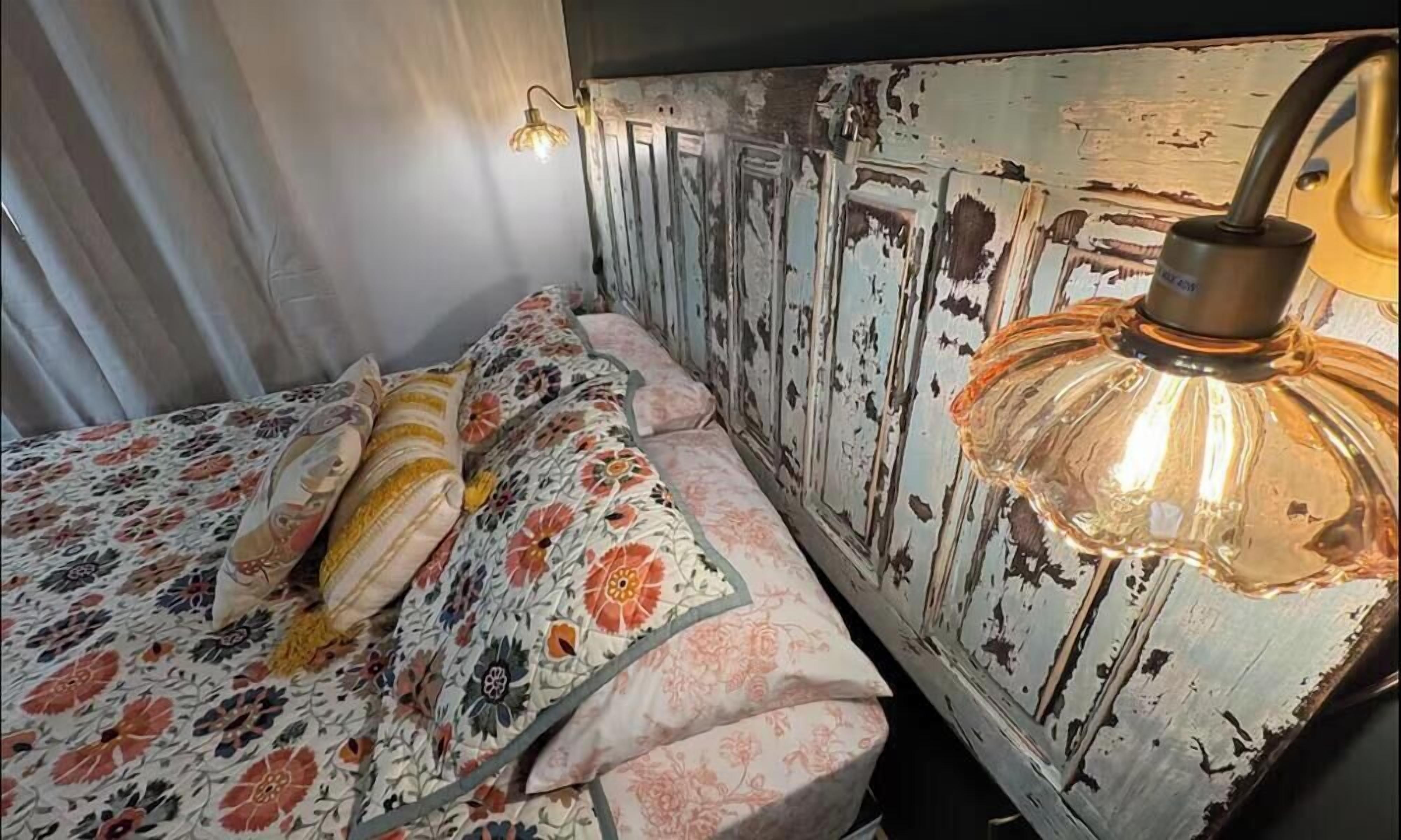 Un lit avec une literie à motifs floraux, un mur à l’aspect vieilli et un luminaire suspendu.