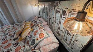 Een bed met bloemenbeddengoed, een verweerde muur en een hangende lamp.
