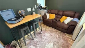 Een kamer met een bruine leren bank, een houten bureau met een platenspeler, een wereldbol en een klein krukje.