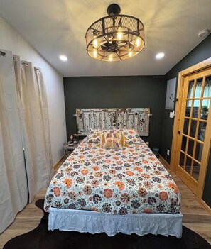 Une chambre à coucher avec une couvre-lit à motifs floraux, une tête de lit ancienne, un ventilateur de plafond et une porte en bois.