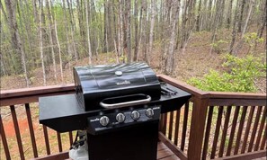 Un barbecue à gaz Char-Broil sur une terrasse en bois, avec une forêt en arrière-plan.