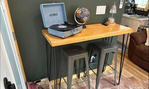 Une pièce avec une table en bois, un tourne-disque, deux tabourets, un globe terrestre et une machine à café.