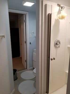 A bathroom with a shower, toilet, and sink. There are two white mats on the floor.