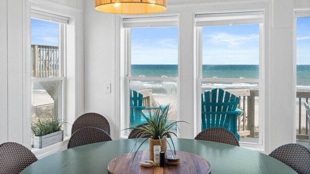 Un comedor con vista al océano, una mesa de madera, sillas y una lámpara colgante.