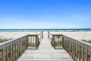Ein hölzerner Steg führt zu einem Strand unter blauem Himmel.