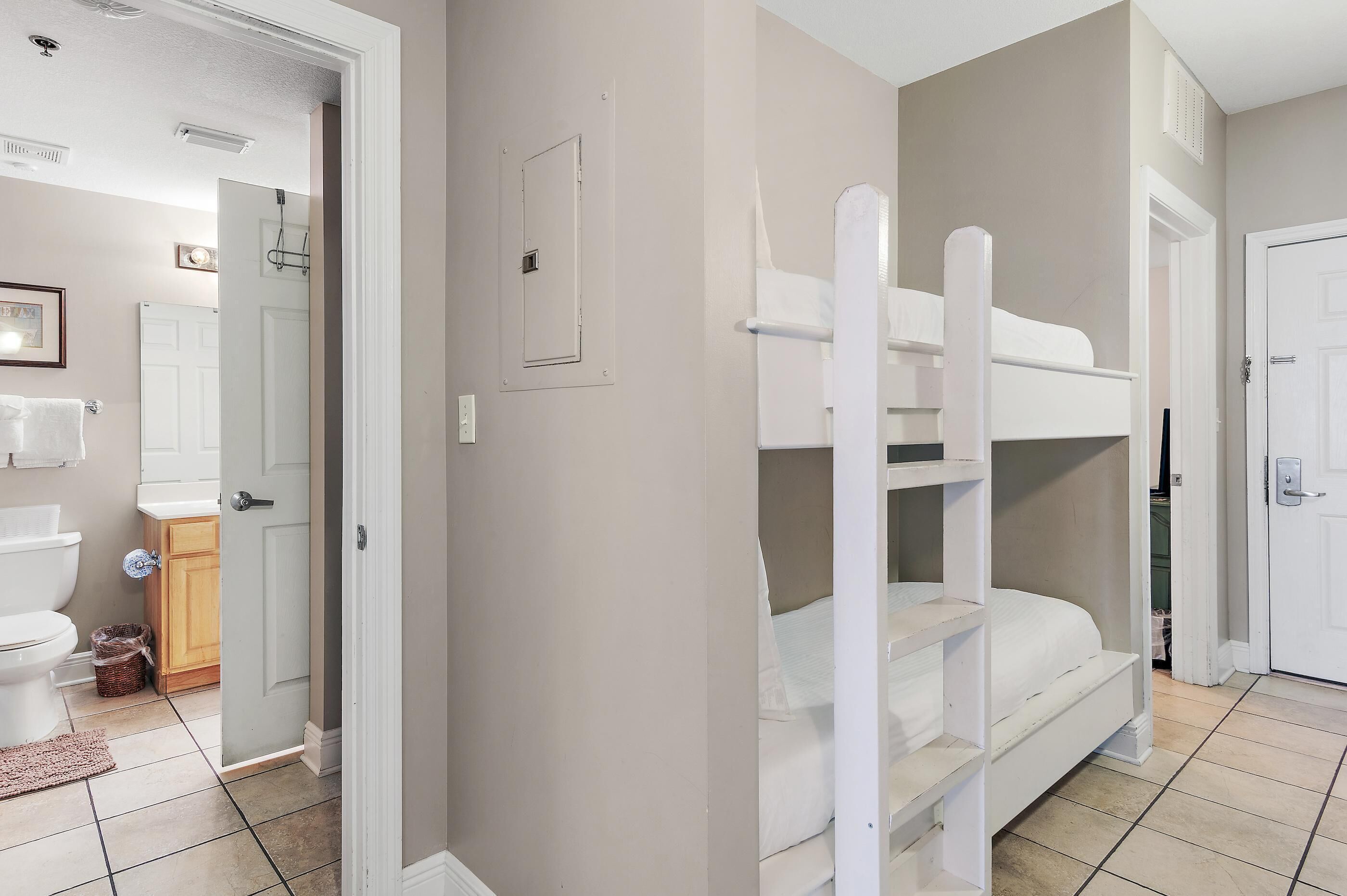 Quarto com beliches, sanita, lavatório e porta para outro espaço.
