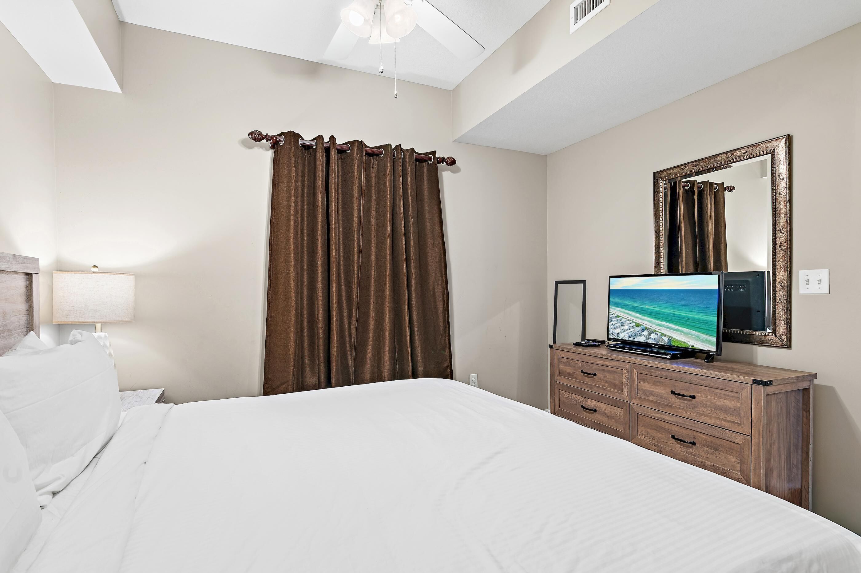 A hotel room with a bed, a TV, a dresser, a mirror, and a window with curtains.