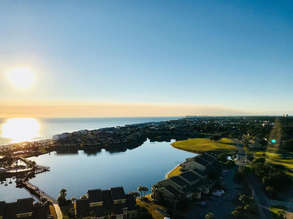 Ett flygbildsbild av ett kustområde med en småbåtshamn, bostadshus och en klar himmel.