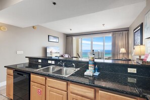 A modern kitchen with a black granite countertop, stainless steel sink, and wooden cabinets. - Ariel Dunes II 1606 (Miramar Beach)