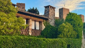 Un edificio storico in pietra con una torre, circondato da una vegetazione rigogliosa.