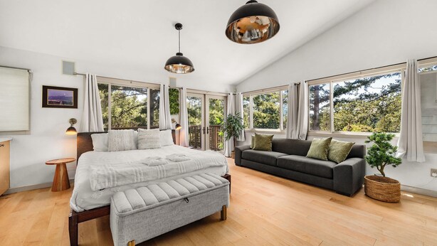 Ein geräumiges Zimmer mit einem großen Bett, einem Sofa und Blick ins Grüne durch große Fenster.