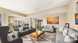 Ein geräumiges Wohnzimmer mit grauen Sofas, einem Holztisch und einem großen abstrakten Gemälde an der Wand.