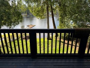 Una terraza de madera con barandilla que da a un lago con un muelle y un bote.