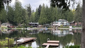 Näkymä järvelle, jossa on laituri, nurmialue ja taustalla näkyviä taloja.
