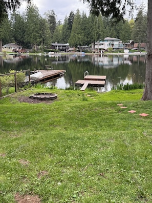 Une vue sur le lac, avec un quai, une zone herbeuse et des maisons en arrière-plan.