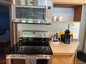 A compact kitchen with a microwave, stove, and a coffee maker. There are white mugs on a shelf, a knife block, and a small refrigerator. - Lakefront Cottage in Kent +hot tub+ firepit+ Canoe (Kent)