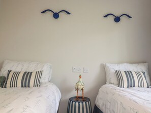A bedroom with two beds, striped pillows, a decorative bird on a stool, and wall-mounted bird-shaped light fixtures. - 67 Manor Villas (St. Columb Major)