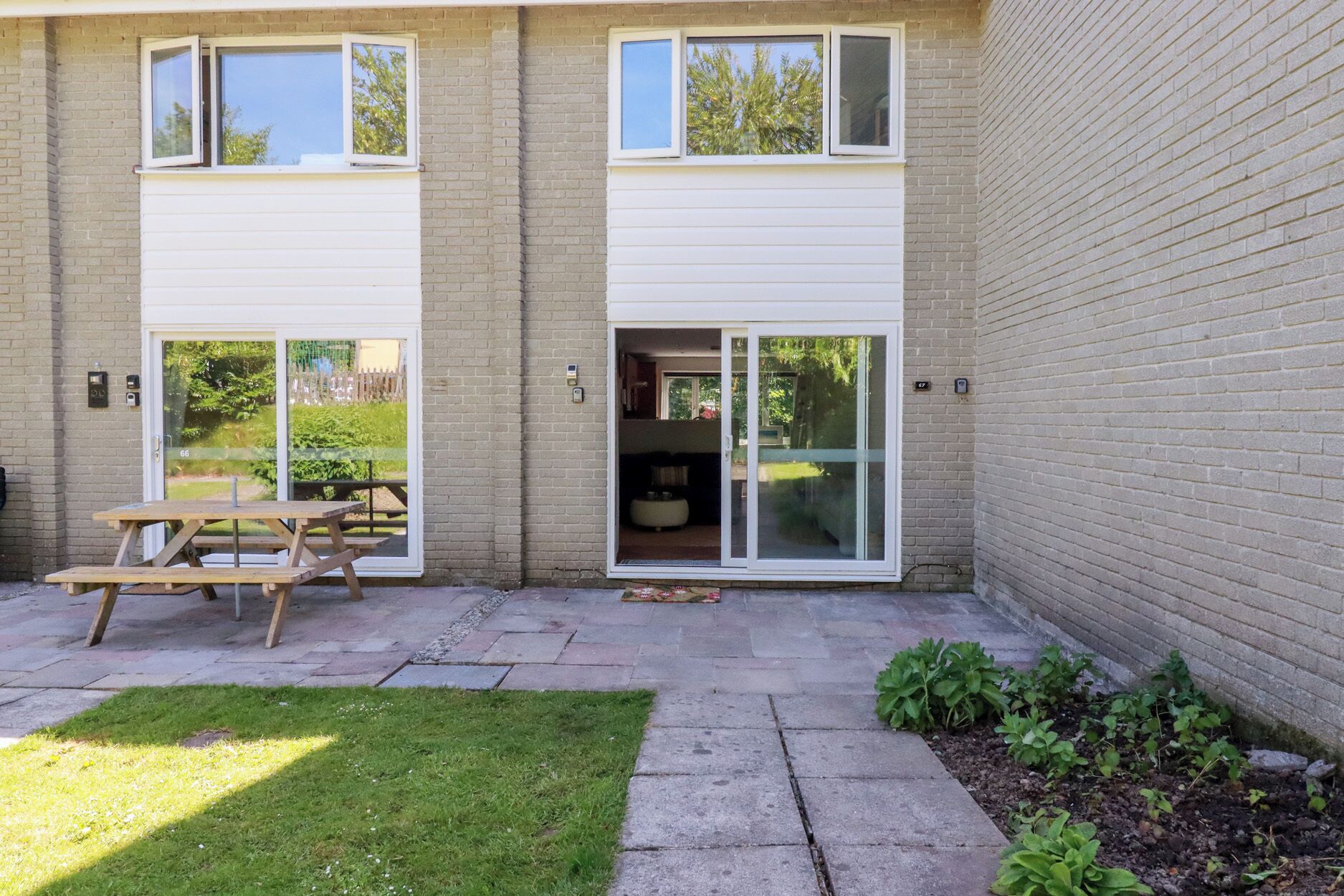 Een gebouw met twee verdiepingen, een patio, een houten picknicktafel en een kleine tuin.