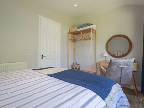A bedroom with a bed, a wooden wardrobe, a round mirror, and a small bedside table. - 67 Manor Villas (St. Columb Major)