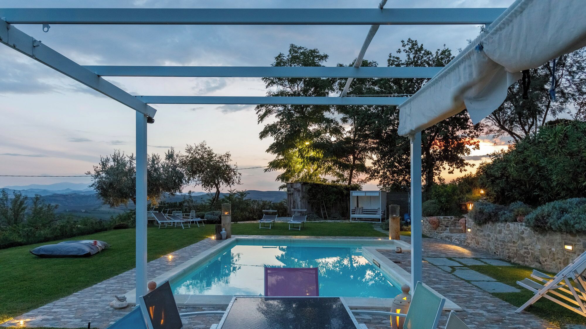 Een zwembadgedeelte met een pergola, lounge stoelen en uitzicht op het landschap.
