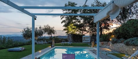 Un área de piscina con un pérgola, sillas de descanso y vistas al paisaje.