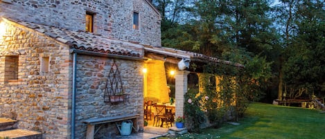A stone building with a tiled roof, a wooden bench, and a table with chairs outside.