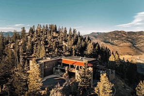 Un bâtiment moderne avec un toit rouge, entouré d’une forêt dense et avec des montagnes en arrière-plan.