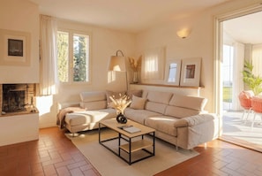 A living room with a sofa, a coffee table, a fireplace, and a view of the outdoors.