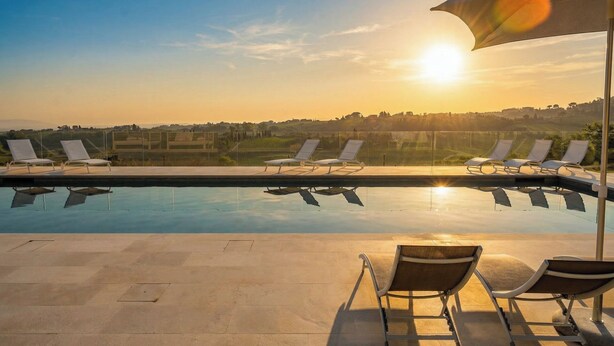 A pool with lounge chairs and an umbrella, overlooking a landscape with buildings and fields. - Villa Oxa 12+2, Emma Villas (Imola)