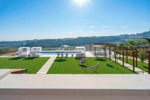 A rooftop terrace with a pool, seating areas, and a view of the countryside.