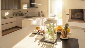 A modern kitchen with a central island, a dining area with a glass-top table, and a fireplace. - Villa Oxa 12+2, Emma Villas (Imola)