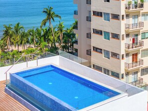 A rooftop infinity pool with a clear view of the ocean and palm trees. - Condo Zona Romantica a block away from the beach. (Puerto Vallarta)