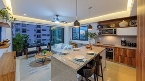 A modern kitchen with a central island, dining area with chairs, and a view of a residential building. - Condo Zona Romantica a block away from the beach. (Puerto Vallarta)
