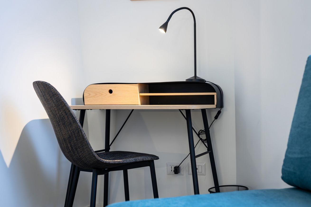 A workspace with a desk, chair, lamp, and power outlet.