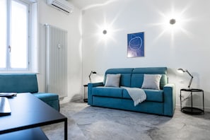A modern living room with a teal sofa, a black coffee table, and a white radiator. - 8 Min walk from the Station, Designer Studio Flat (Milan)