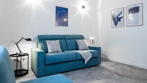 Ett modernt vardagsrum med en blå soffa, ett litet sidobord och väggmonterad belysning.