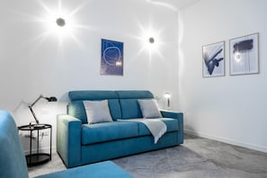 A modern living room with a blue sofa, a small side table, and wall-mounted lighting. - 8 Min walk from the Station, Designer Studio Flat (Milan)