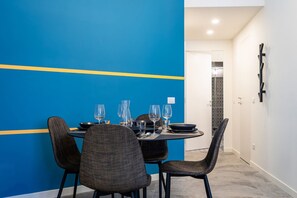 Ein Essbereich mit einem runden Tisch, gedeckt für vier Personen, umgeben von Stühlen. Im Hintergrund eine Wand in Blautönen und eine weiße Tür.
