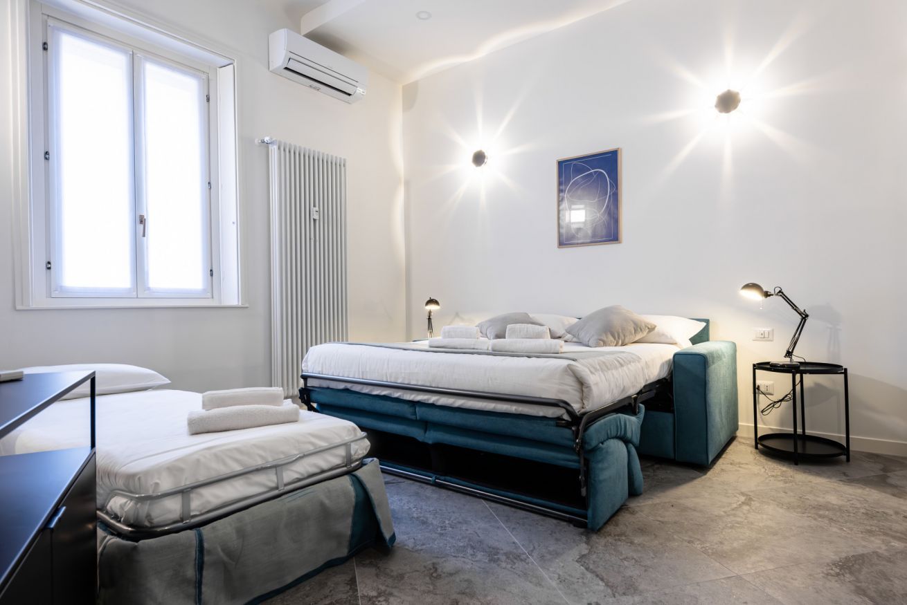 A bedroom with a bed, a desk, a chair, a radiator, and a window.