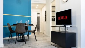 Ett modernt vardagsrum med en matplats, en tv på ett tv-bord och en klocka på väggen.