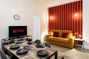 A modern living room with a dining area, a sofa, a TV displaying 'NETFLIX,' and a wall with vertical red stripes. - 8 Min walk from the station and Corso Buenos Aires (Milan)