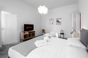 Ein modernes Hotelzimmer mit einem Bett, zwei Nachttischen, einem Fernseher, einem Sessel und einem Schreibtisch.