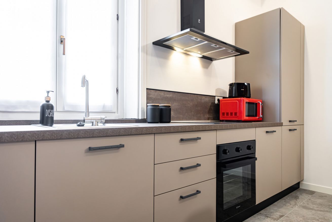 A modern kitchen with a built-in oven, a red microwave, and a window with a view.