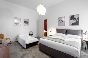 Et moderne hotelværelse med to senge, et skrivebord, en stol, en hængende lampe og kunst på væggene.