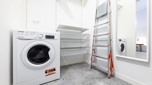 Een wasserette met een voorlader wasmachine, metalen schappen en een metalen trap.